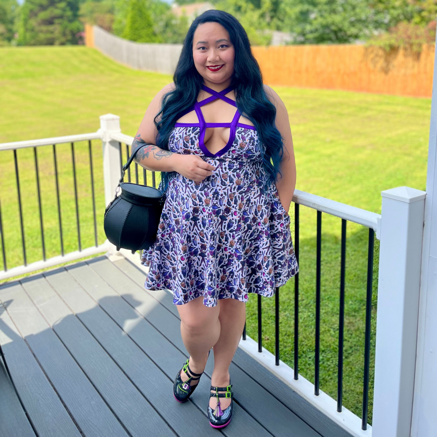Woman in a floral dress with purple accents standing on a deck with green grass and trees in the background.