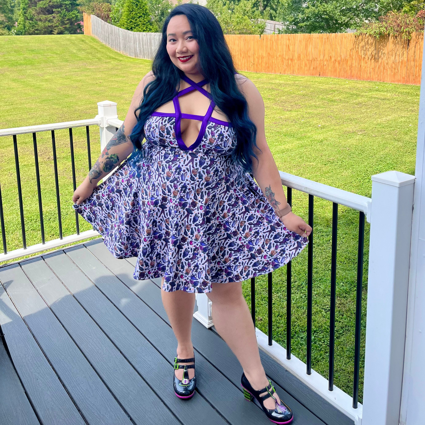 Woman in a floral dress with purple accents standing on a deck with grass and trees in the background