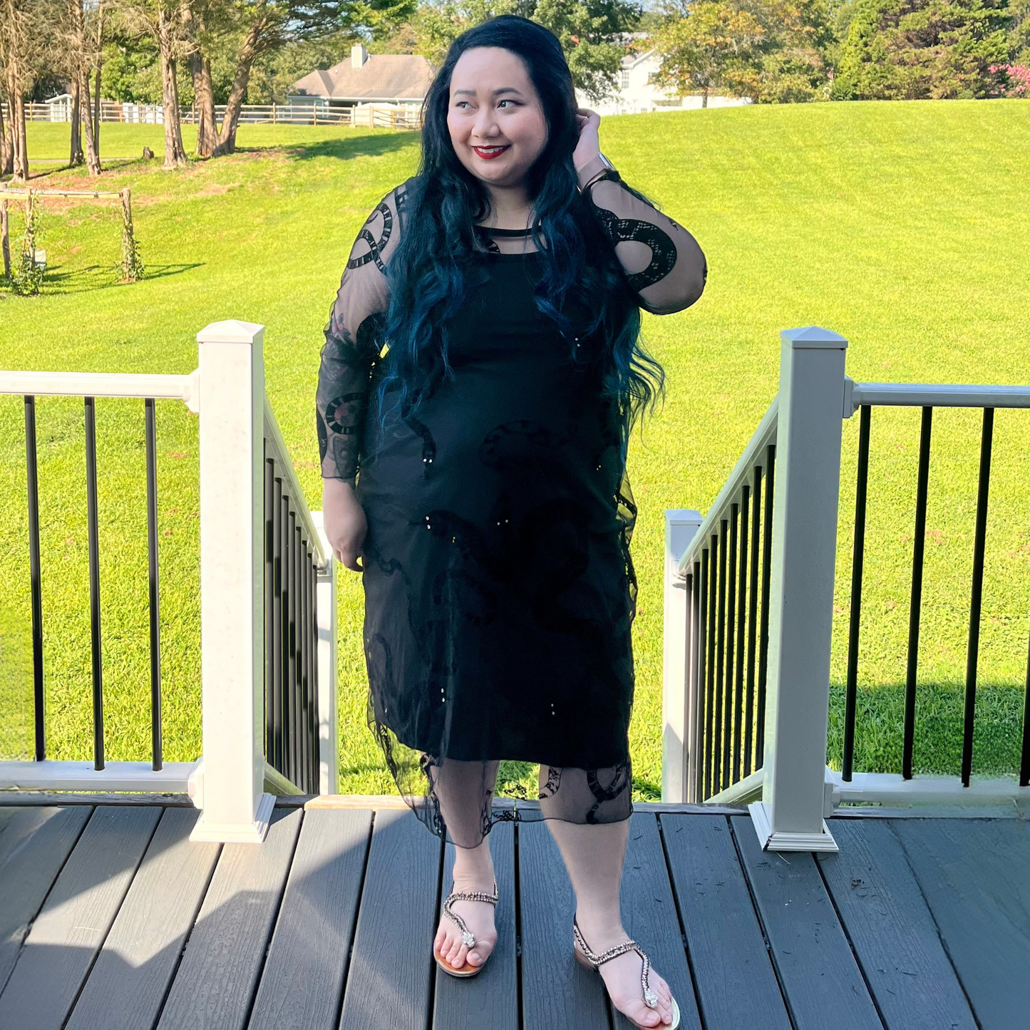 Woman in a black dress standing on a deck with green grass and trees in the background