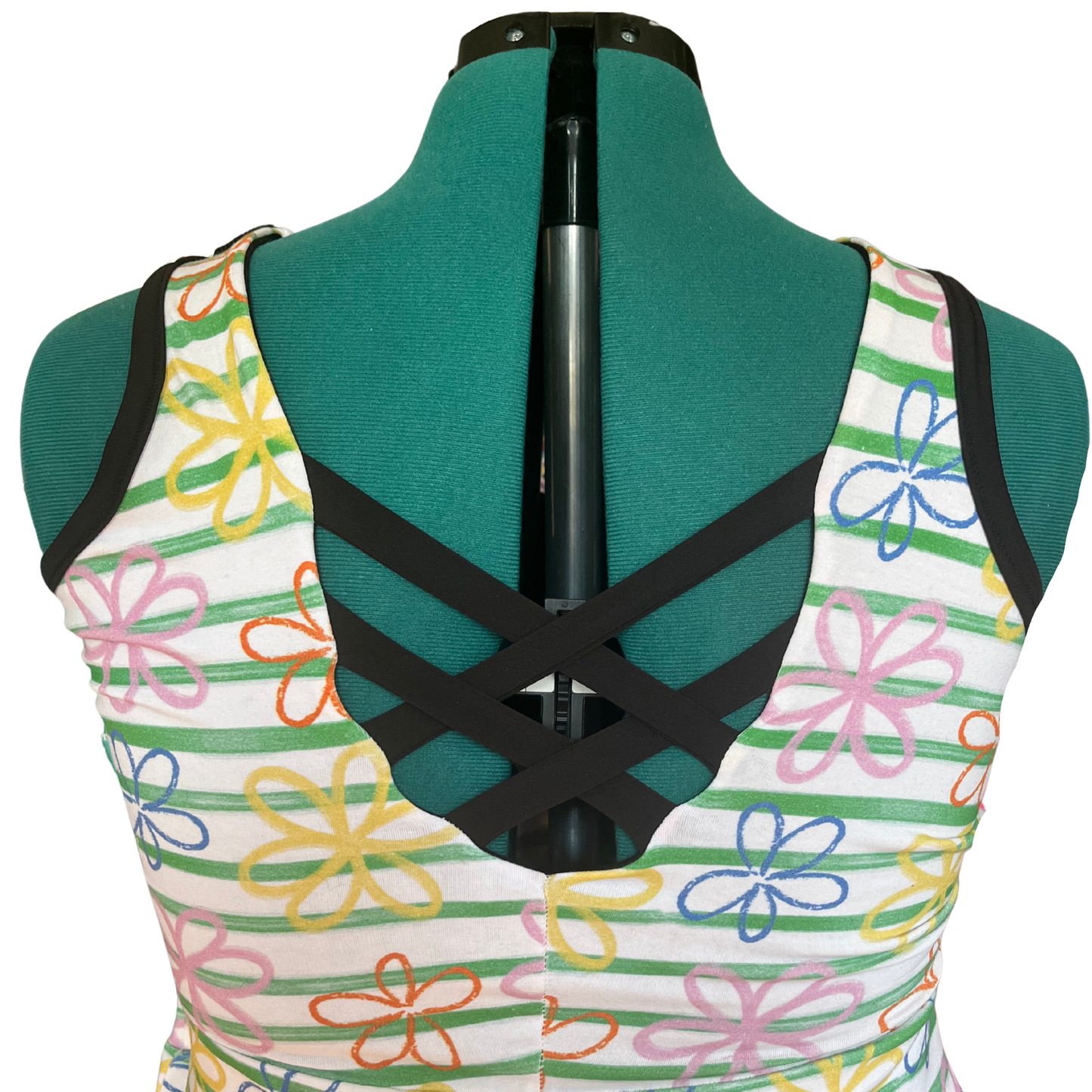 A sleeveless strappy top displayed on a green dress form, featuring a white base with colorful floral patterns and green horizontal stripes.