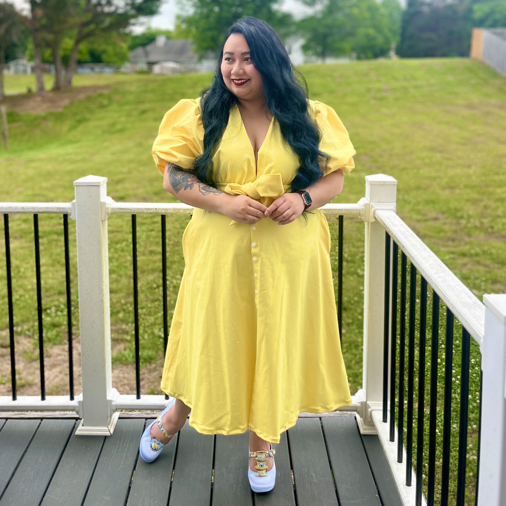 Woman in a yellow dress standing on a deck with a grassy area in the background
