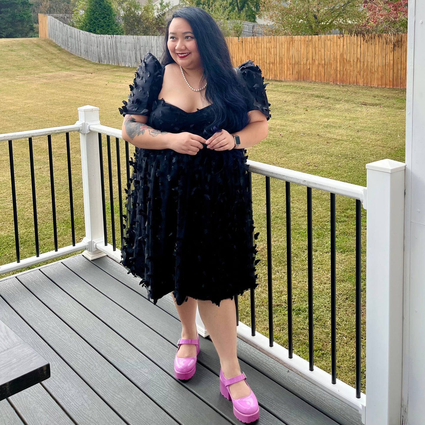 Woman in a black dress with butterfly details standing on a deck.