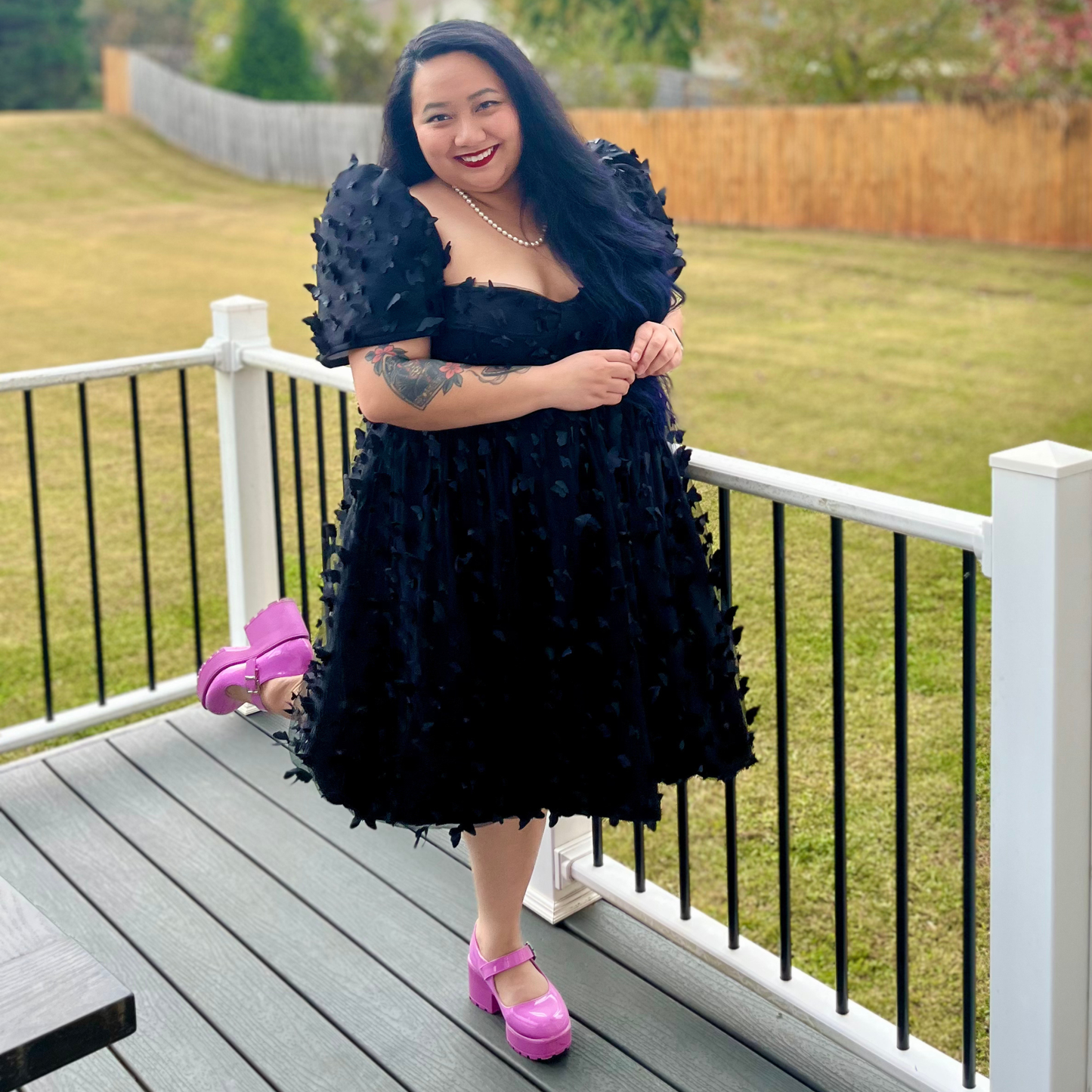 Woman in a black dress with pink shoes standing on a deck.
