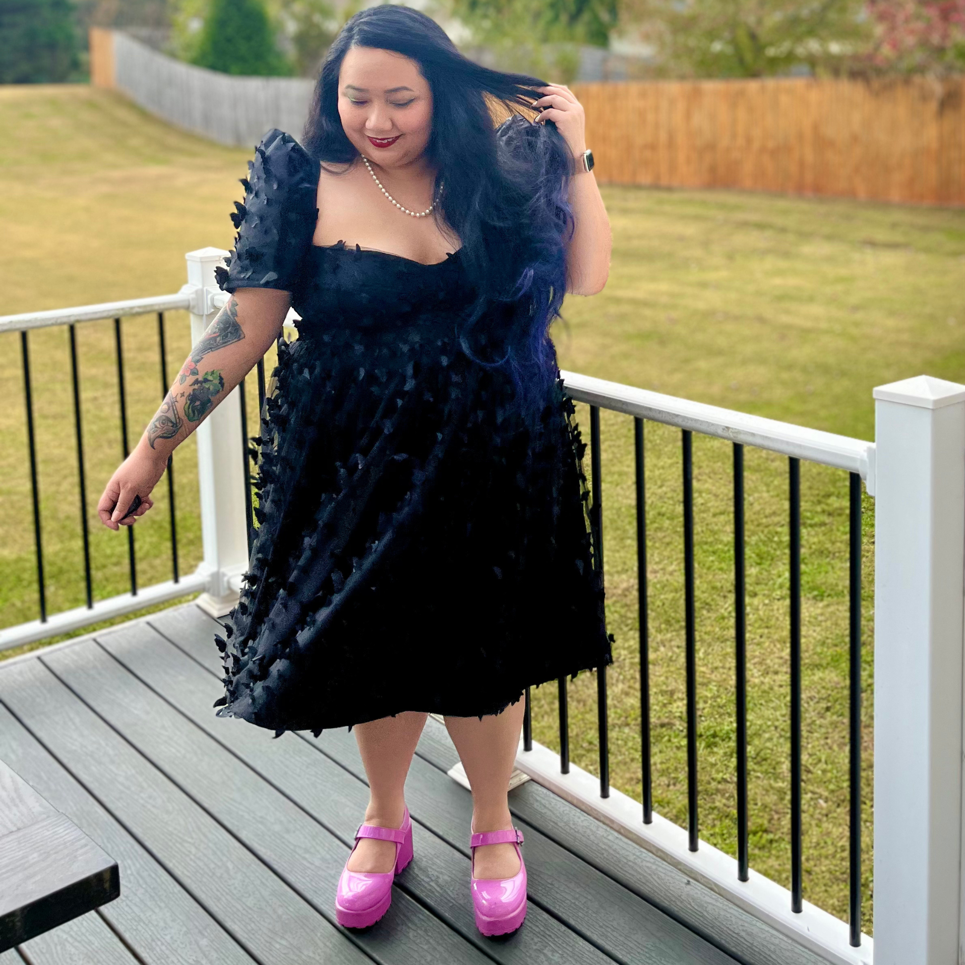 Woman in a black dress with butterfly details standing on a deck.