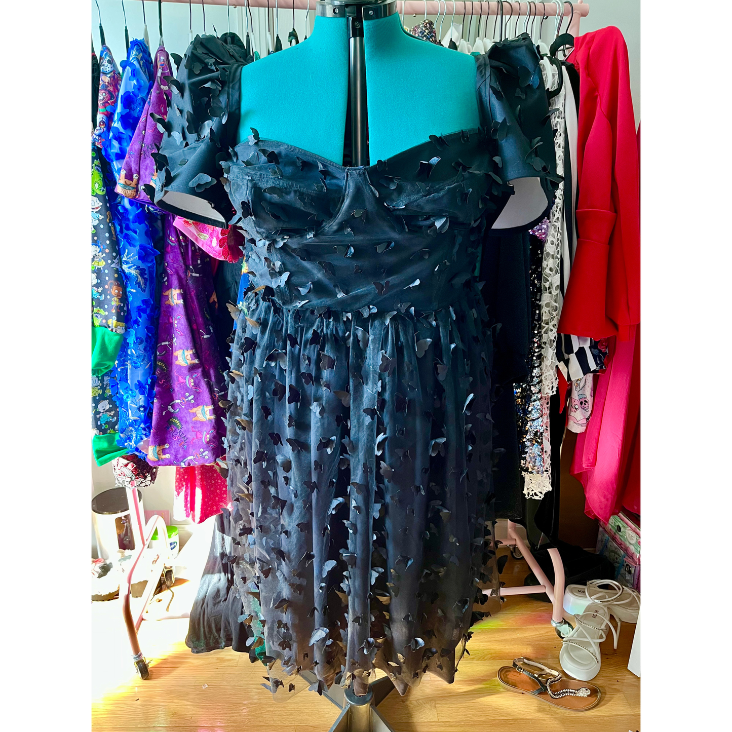 Black dress with unique design on a mannequin against a colorful clothing background