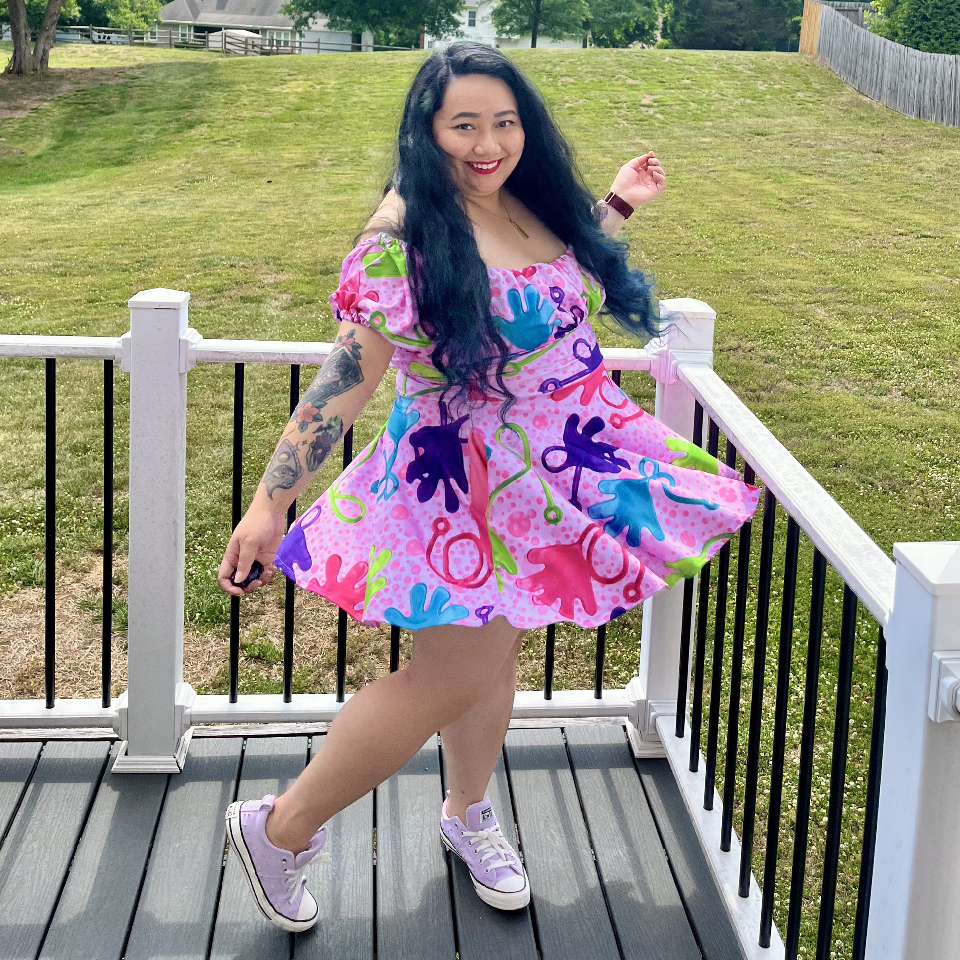 Woman in a colorful dress standing on a deck with grass and trees in the background
