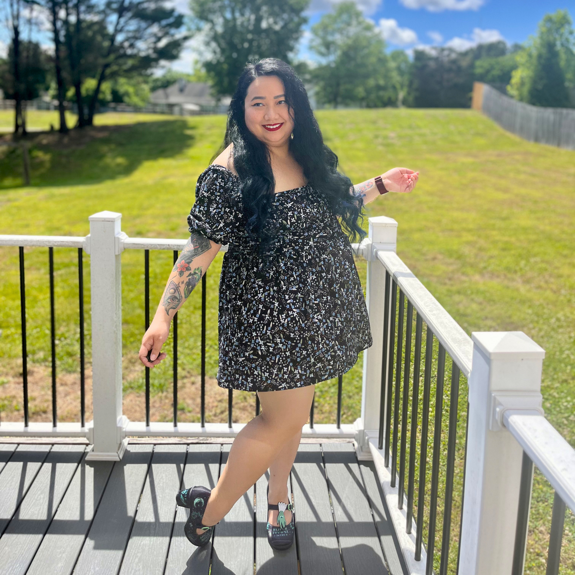 Woman wearing a floral dress standing on a deck in front of grass and trees