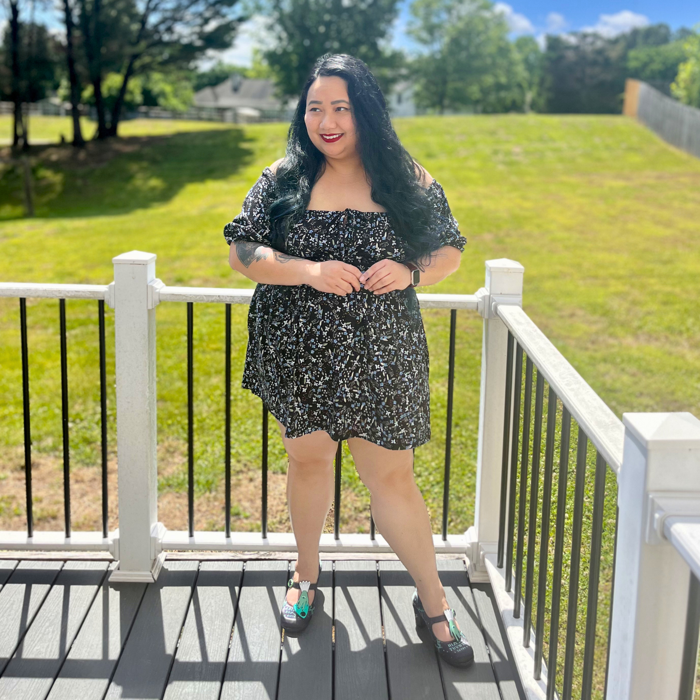 Woman wearing a floral dress standing on a deck in front of grass and trees