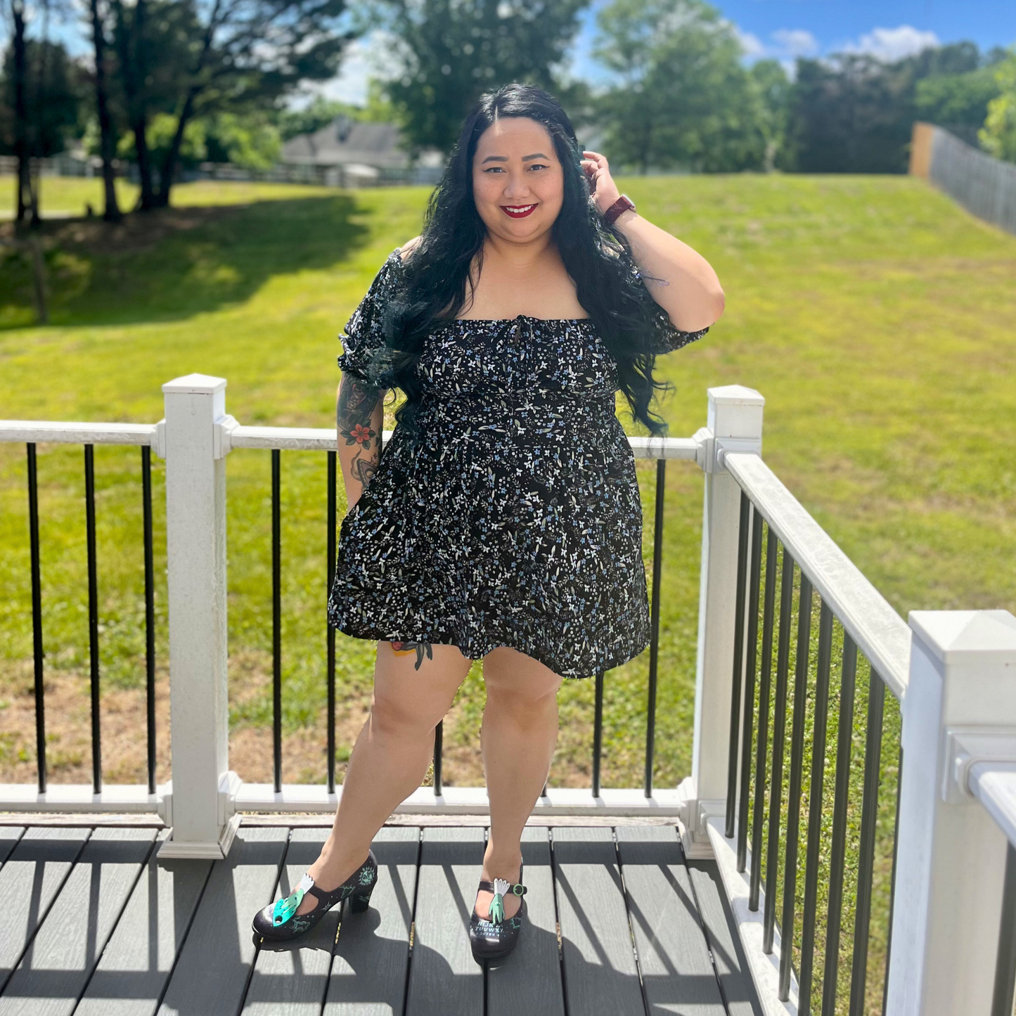 Woman wearing a floral dress standing on a deck in front of grass and trees