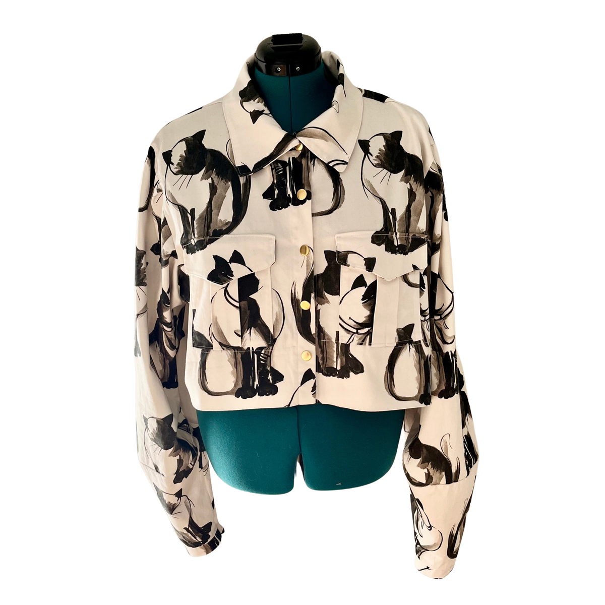 A cropped button-up shirt jacket featuring a black and white cat print, displayed on a teal mannequin torso against a white background.