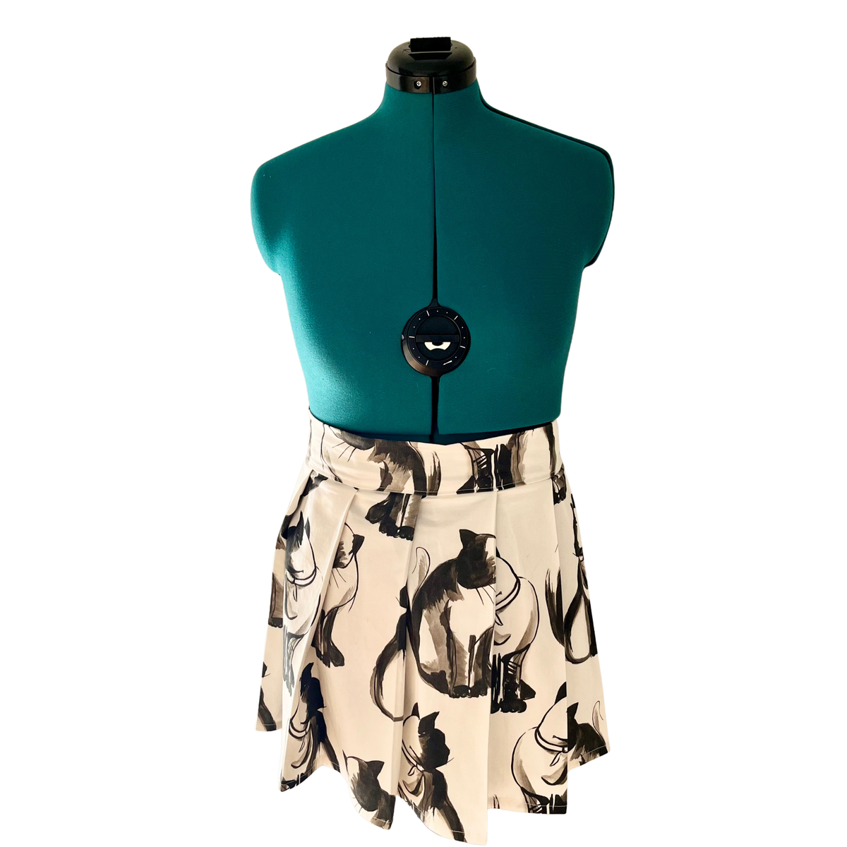 A pleated A-line skirt with a black and beige cat print, displayed on a teal dress form mannequin against a white background.