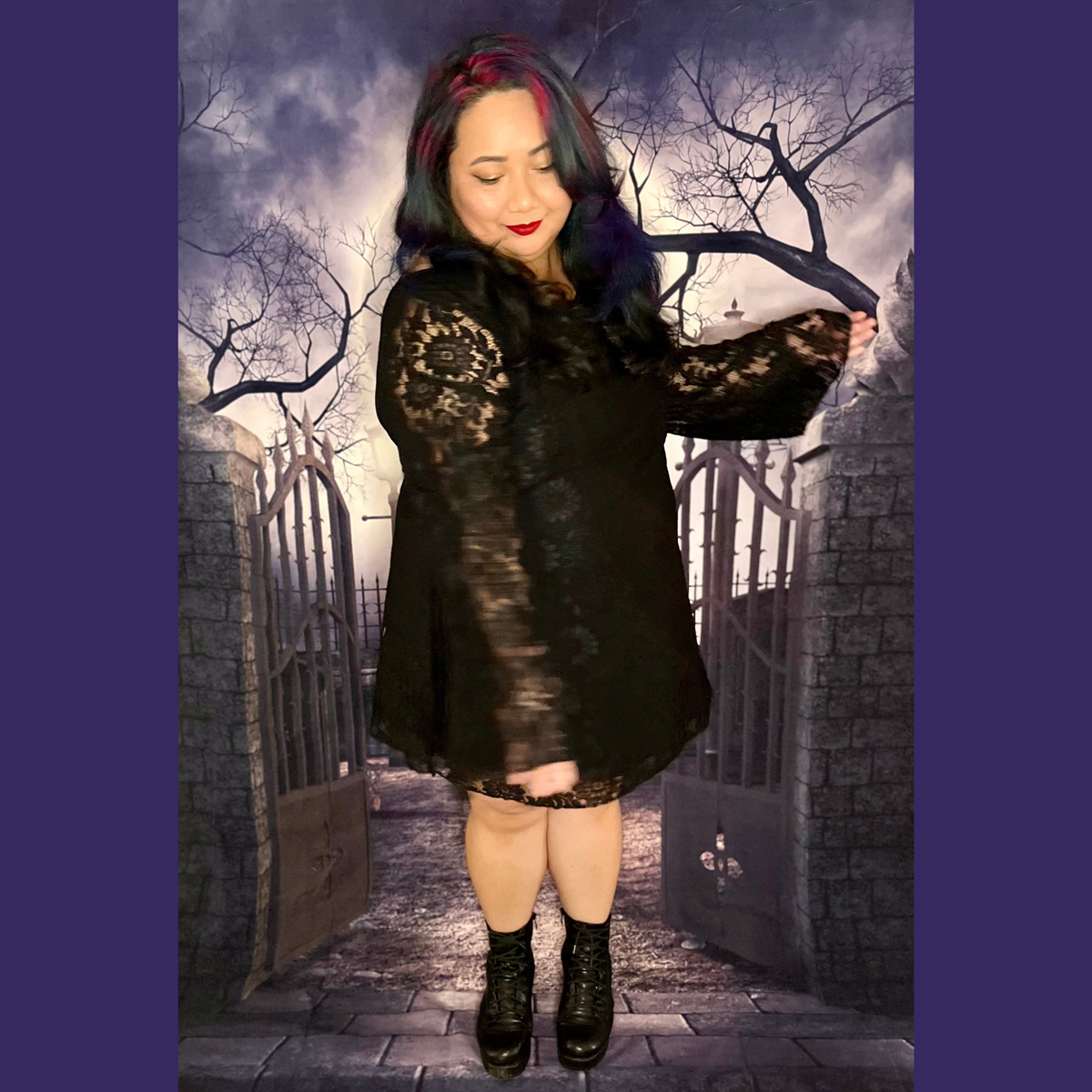 A woman modeling a black lace long-sleeve dress with black lace-up ankle boots, posed in front of a digital background depicting a gothic stone gate and bare trees at night.
