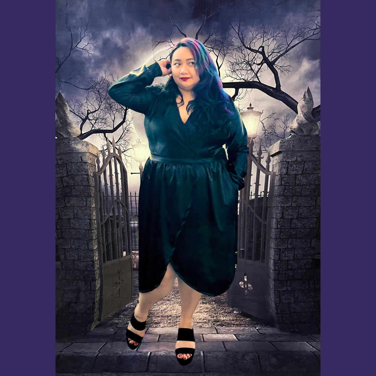 A woman modeling a black wrap-style dress in a gothic cemetery setting with stone gates and bare trees. The dress has long sleeves, a V-neckline, and a gathered waist.