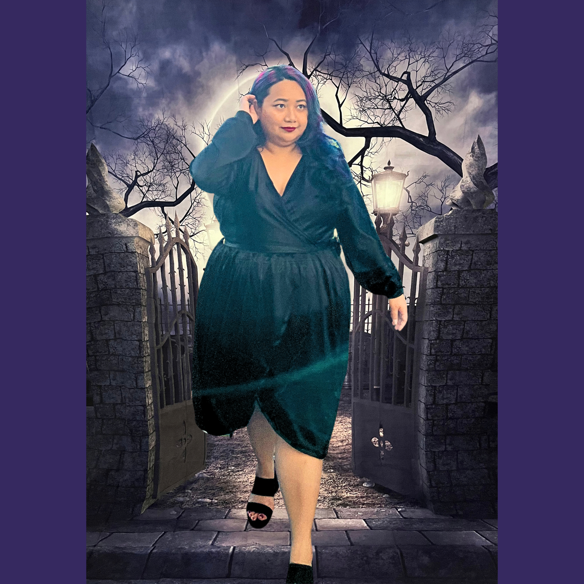 A woman modeling a black wrap-style dress in a gothic cemetery setting with stone gates and bare trees. The dress has long sleeves, a V-neckline, and a gathered waist.
