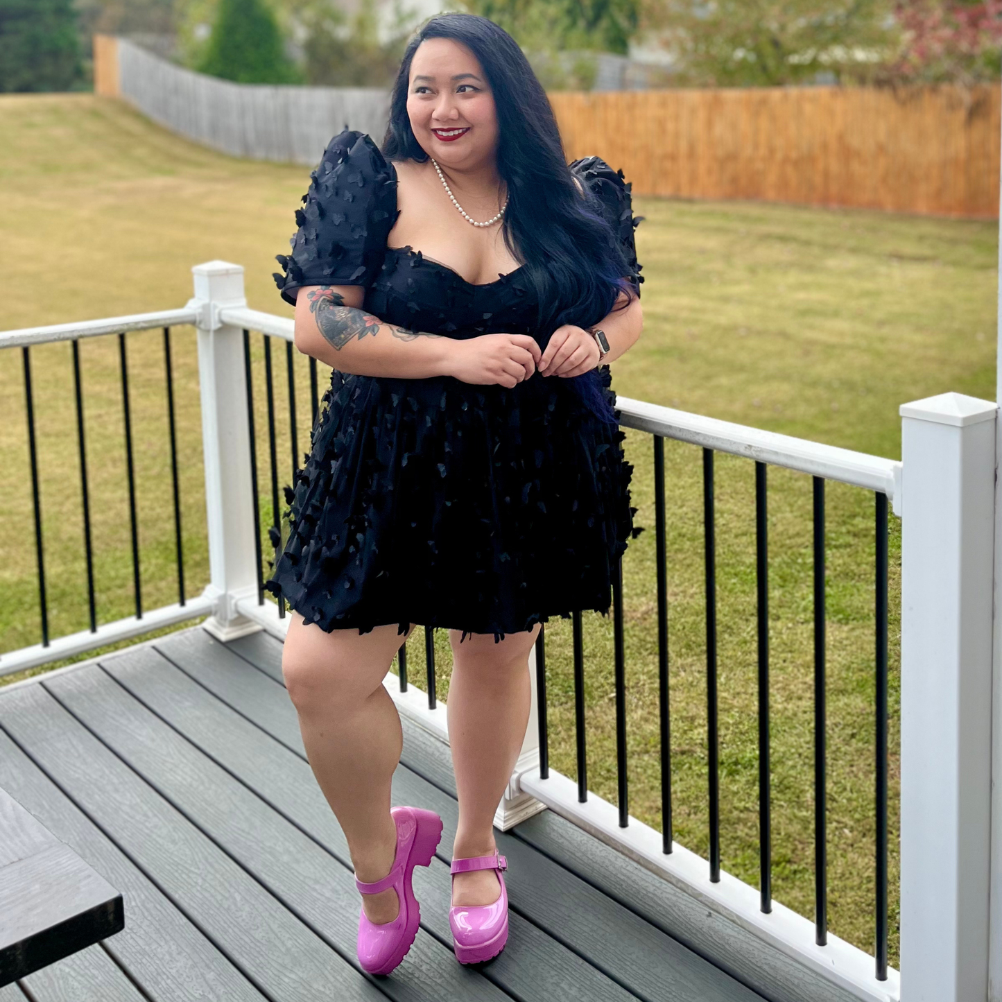 Woman in a black dress with butterfly details standing on a deck.