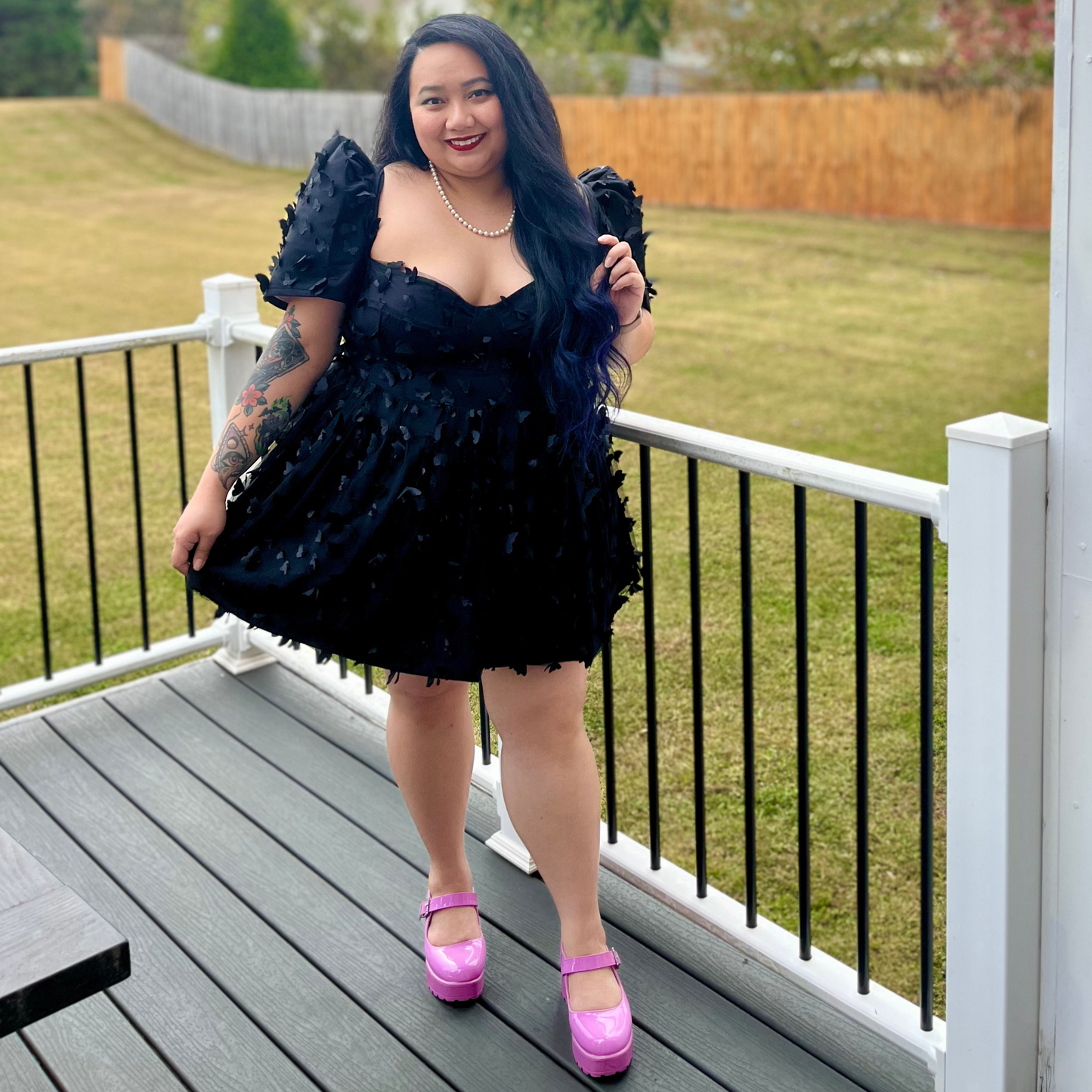 Woman in a black dress with ruffles standing on a deck.