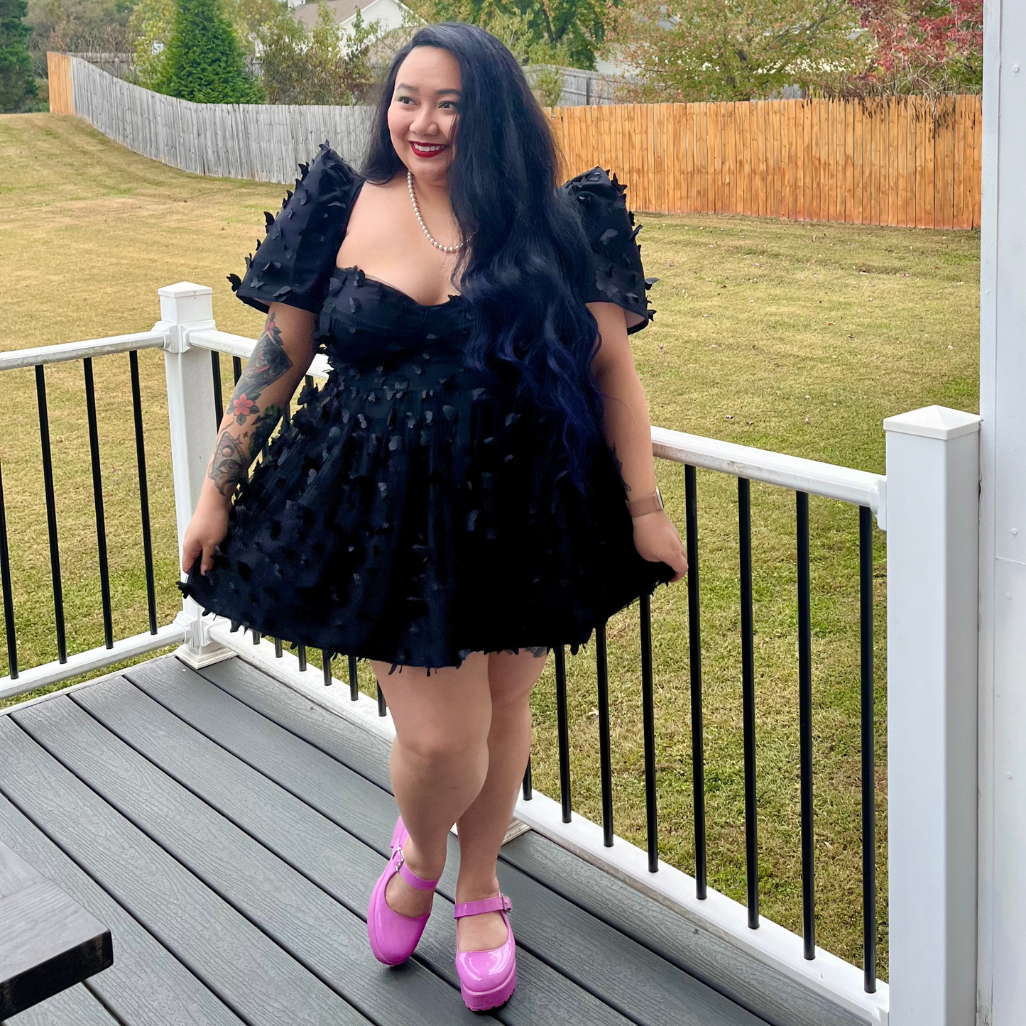 Woman in a black ruffled dress with pink shoes standing on a deck.