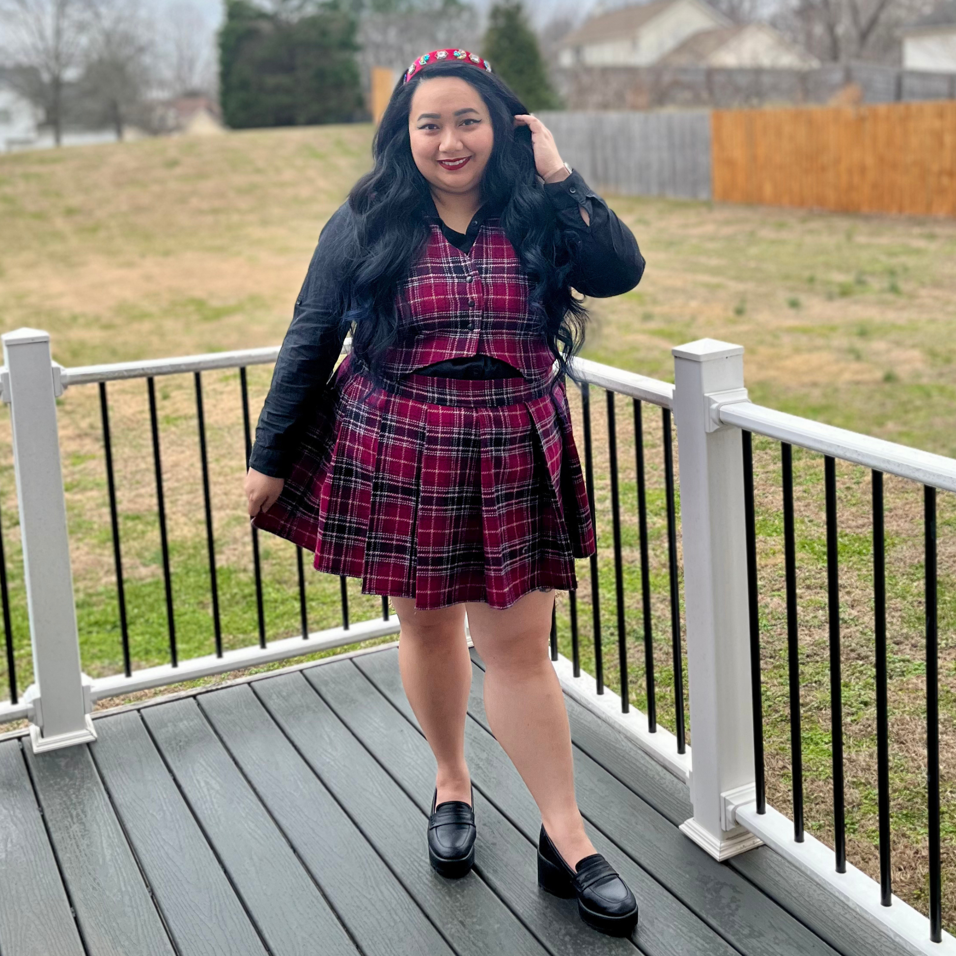 Woman in a plaid dress standing on a deck with a grassy area and fence in the background
