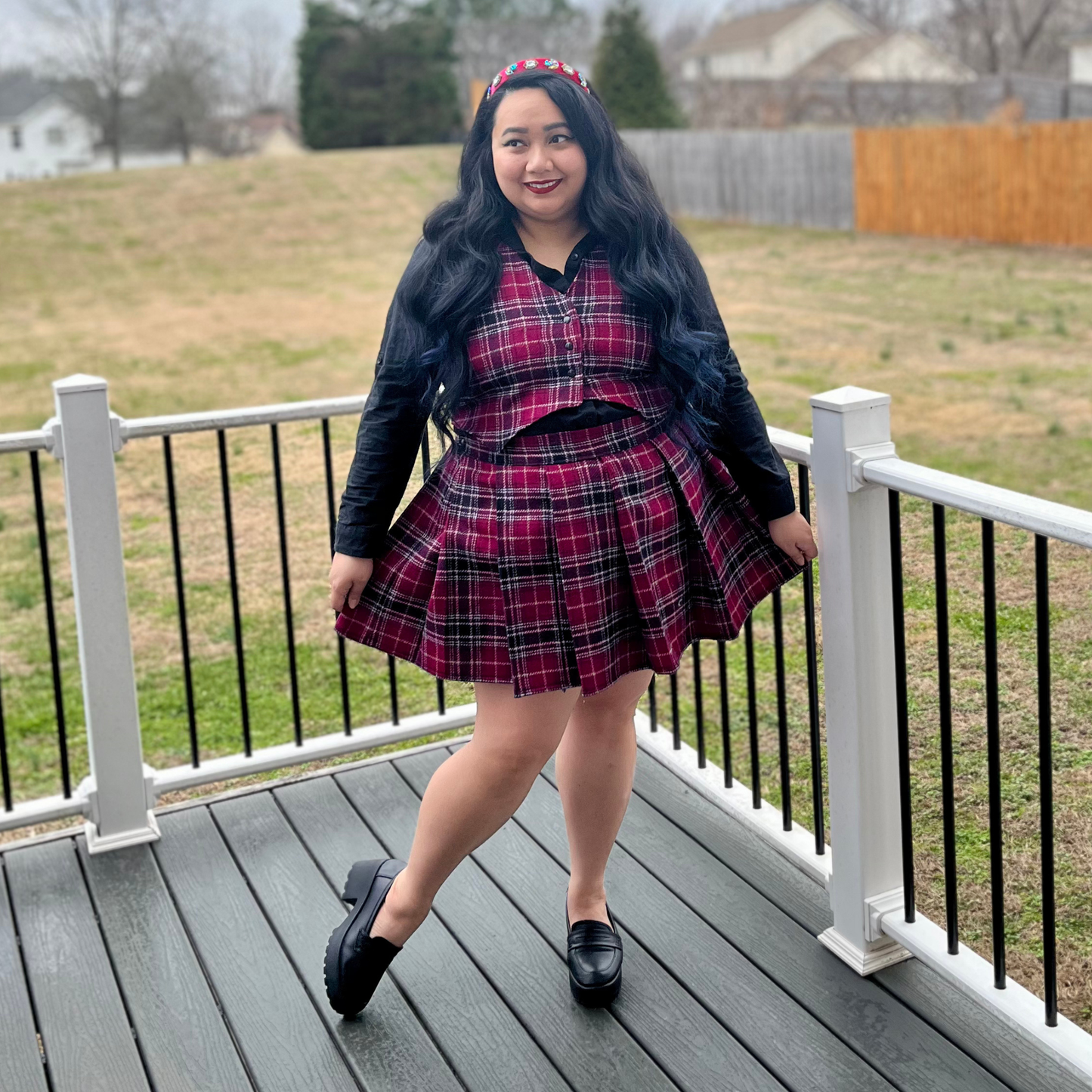 Woman in a plaid dress standing on a deck with a grassy area and fence in the background