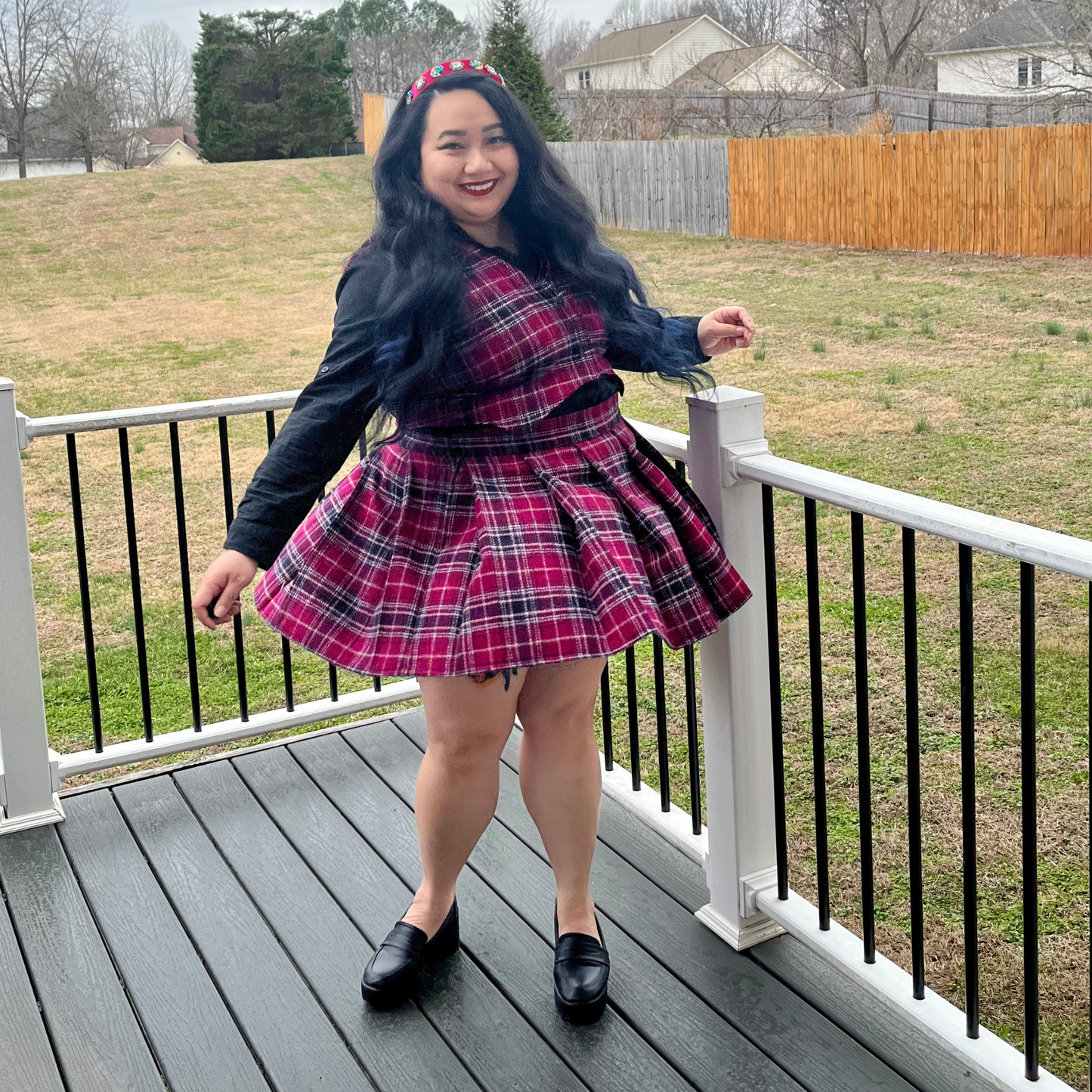 Person wearing a pink plaid dress on a deck with a grassy area and fence in the background
