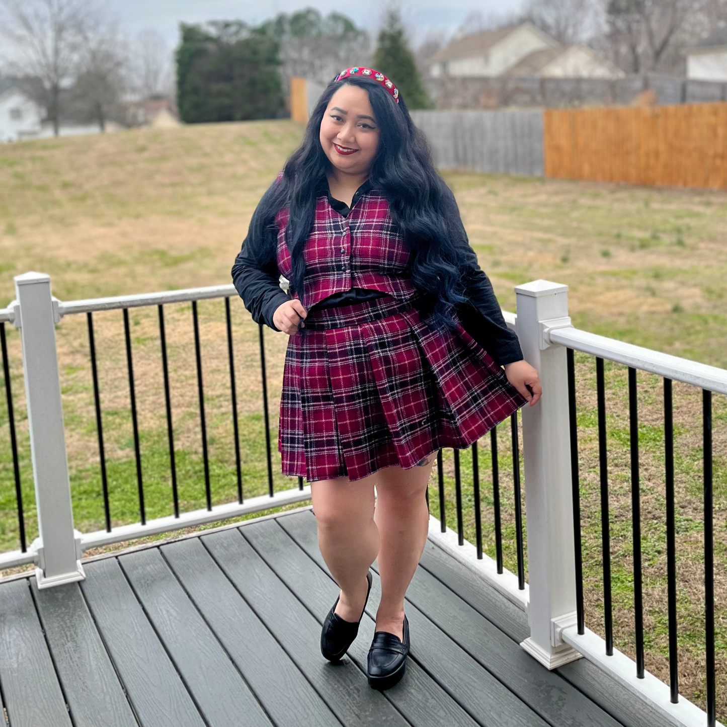Woman in a plaid outfit standing on a deck with grass and trees in the background