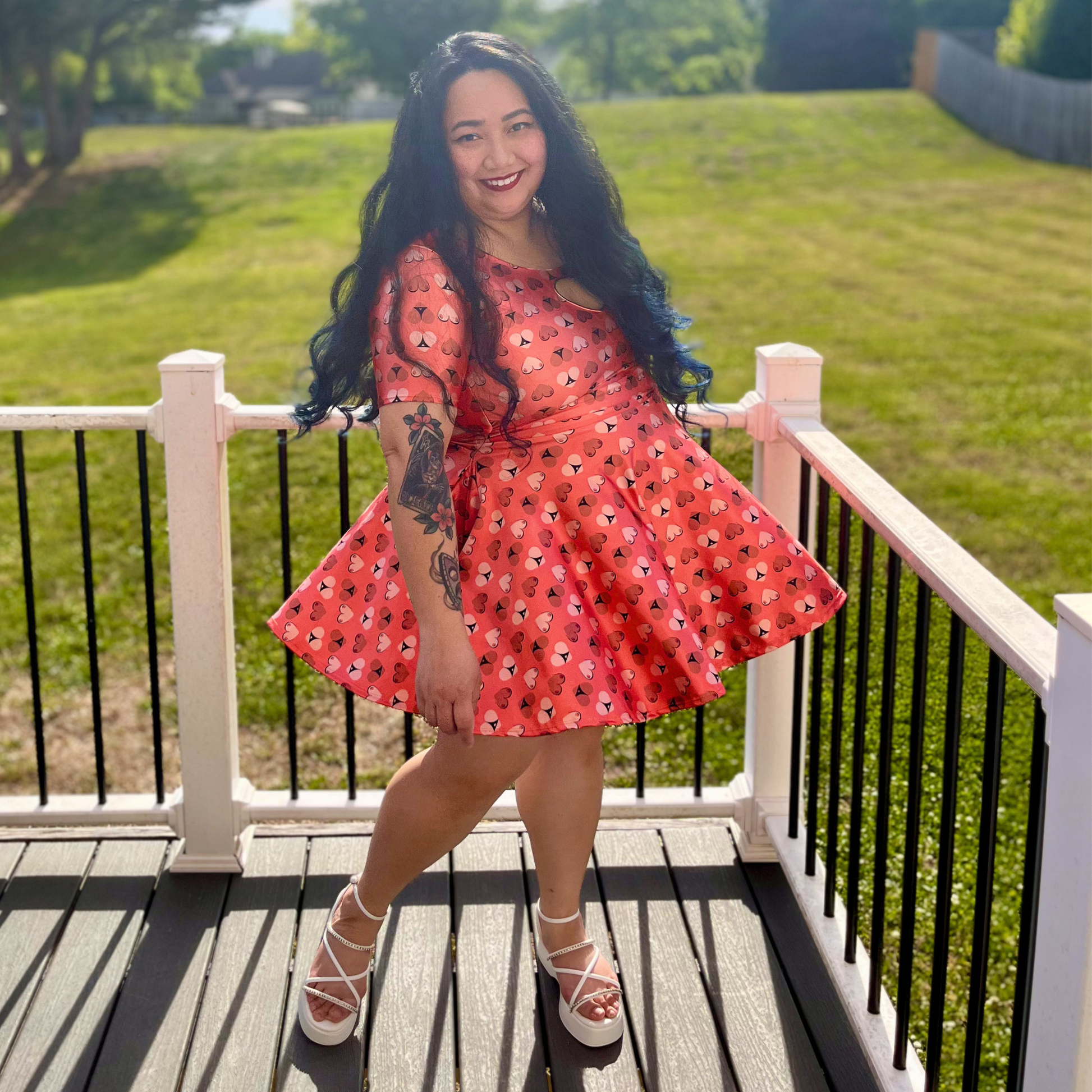 woman in an orange printed dress standing on a deck in front of grass and trees