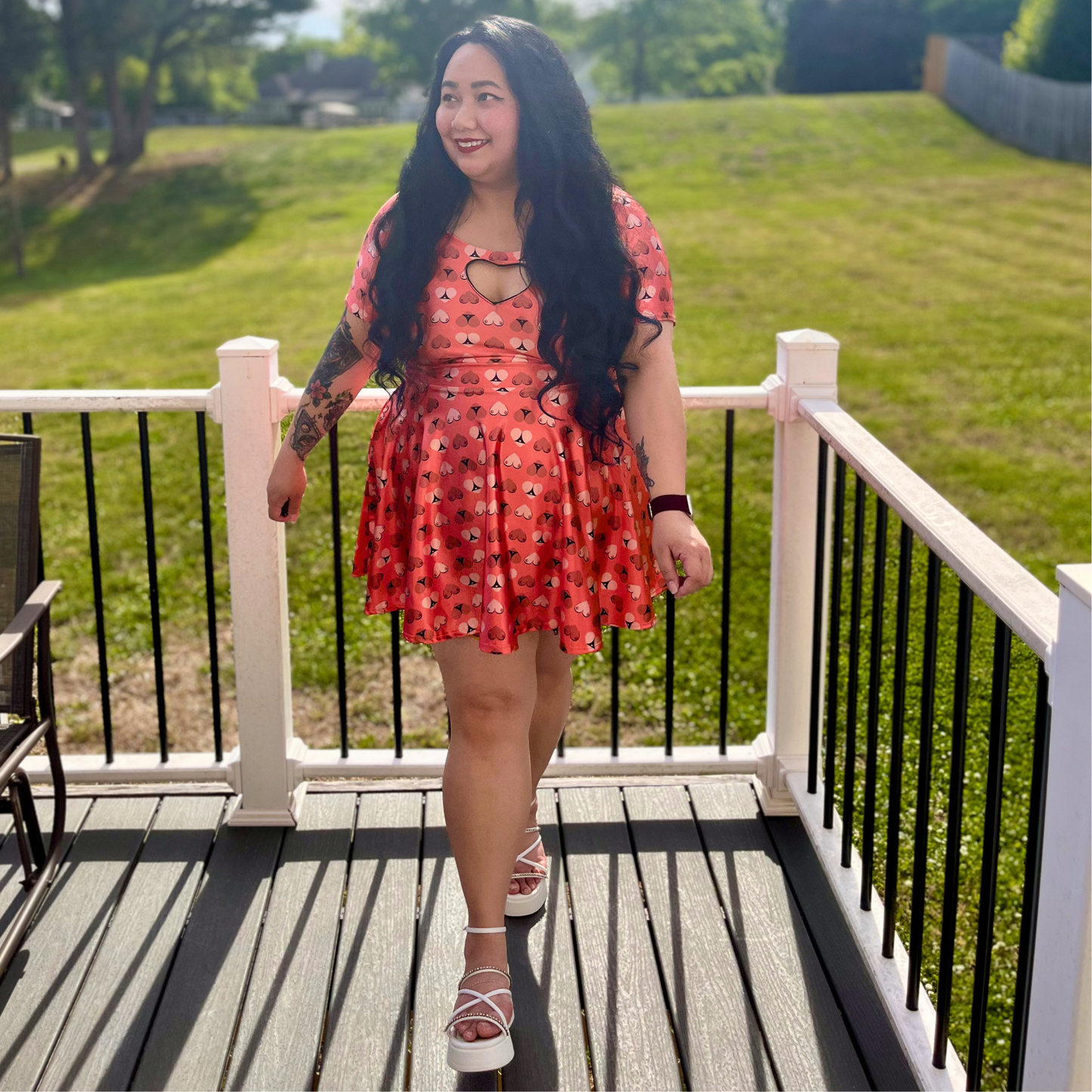 woman in an orange printed dress standing on a deck in front of grass and trees