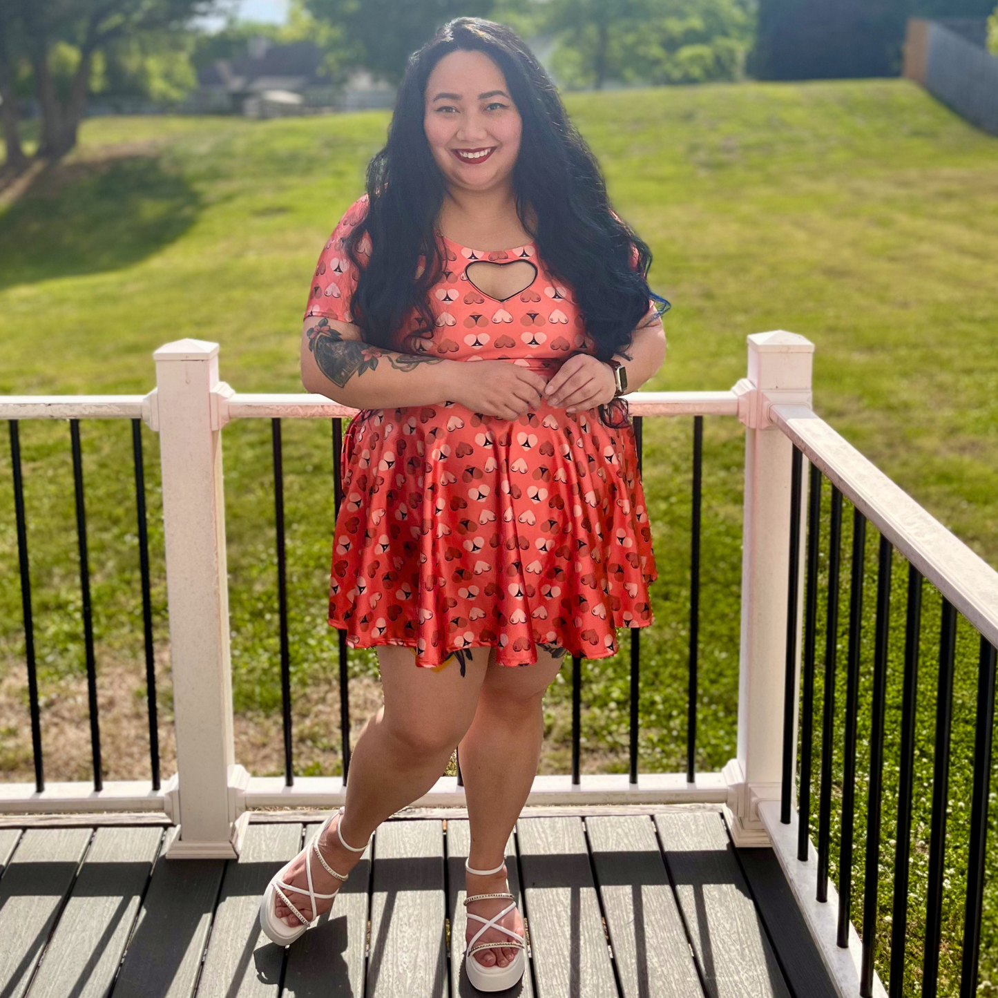 woman in an orange printed dress standing on a deck in front of grass and trees