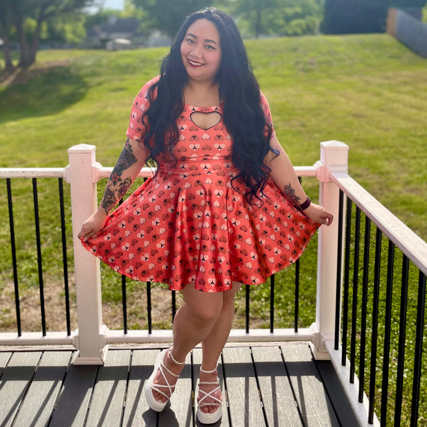 woman in an orange printed dress standing on a deck in front of grass and trees