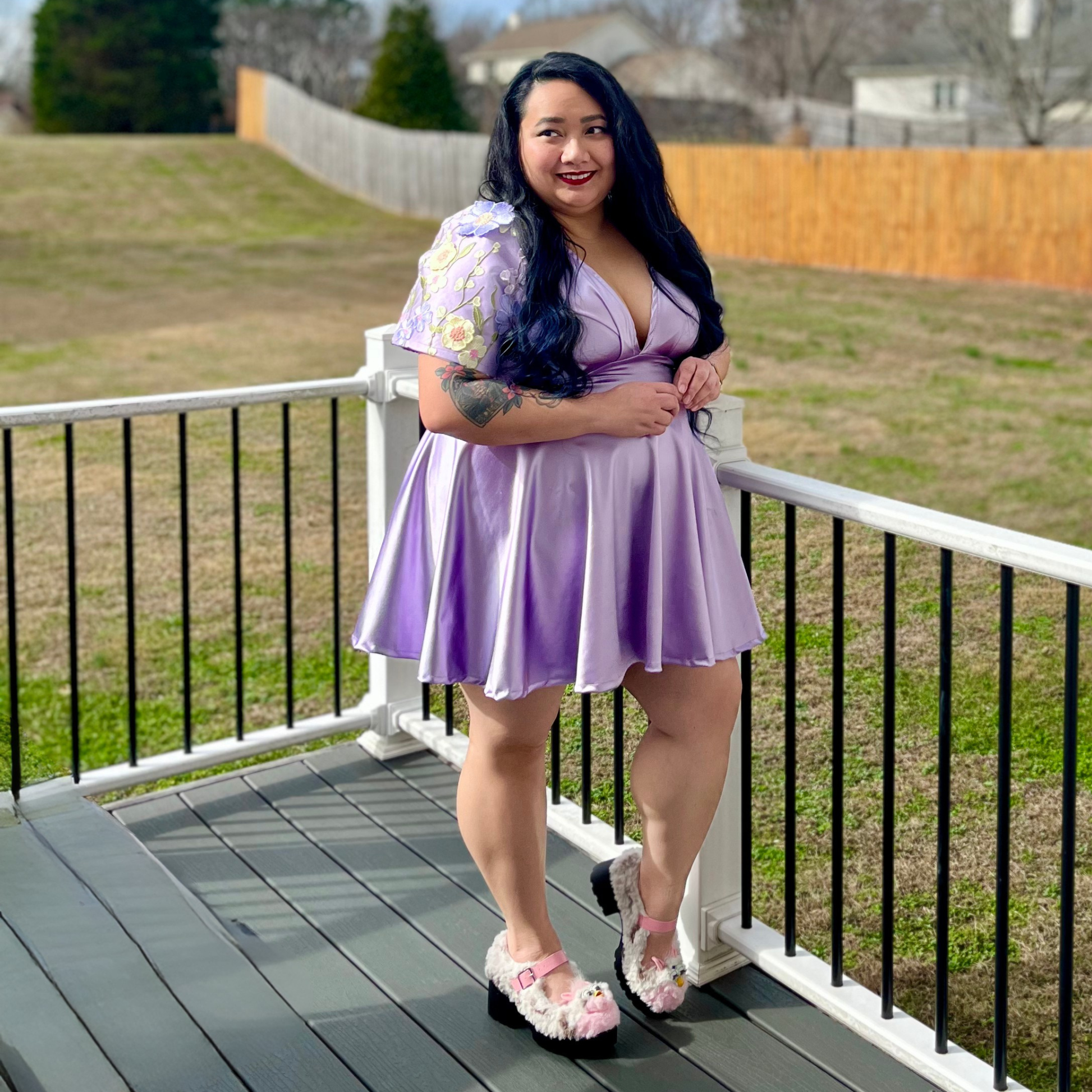 Woman in a purple dress standing on a deck with grass and trees in the background