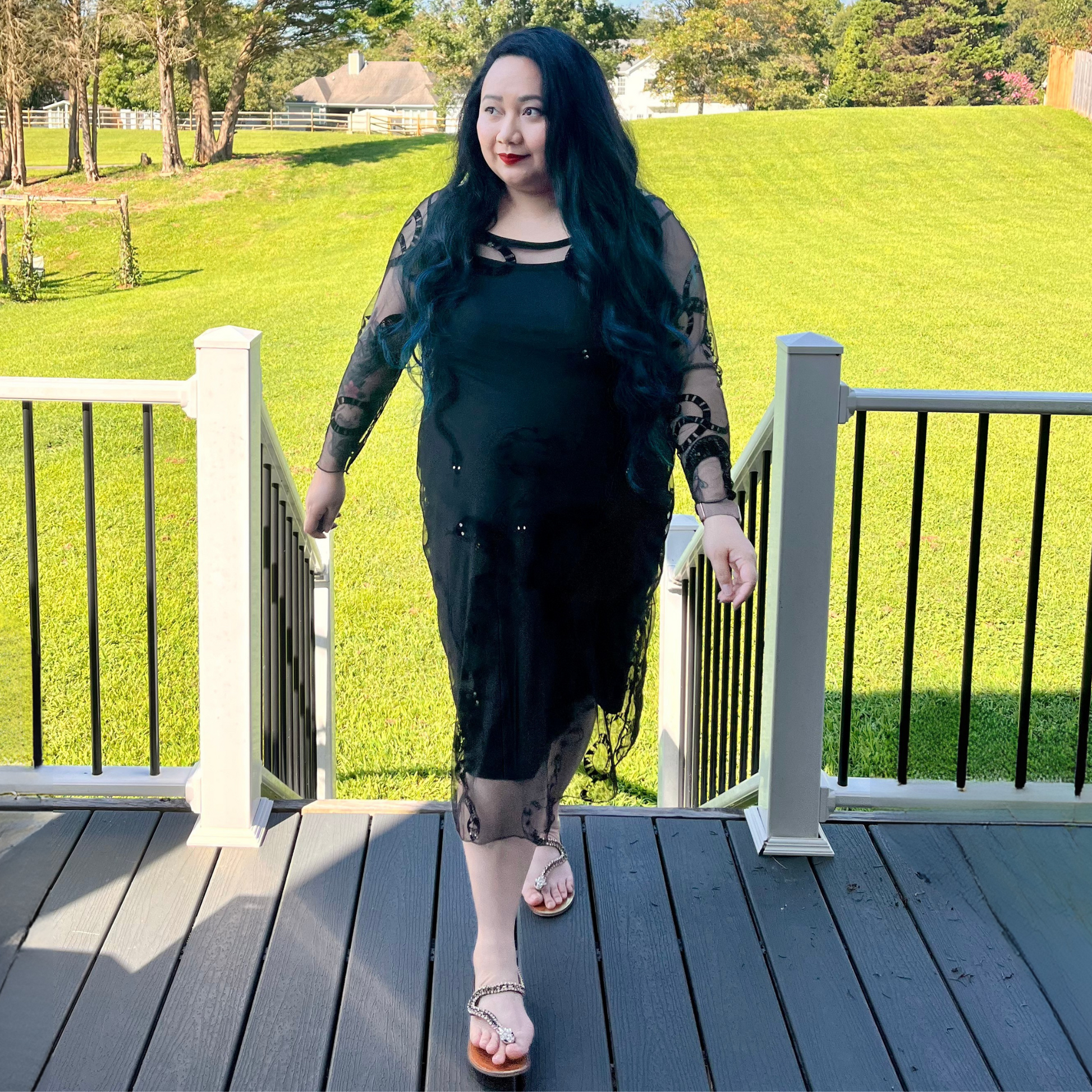 Woman in a black dress standing on a wooden deck with green grass and trees in the background