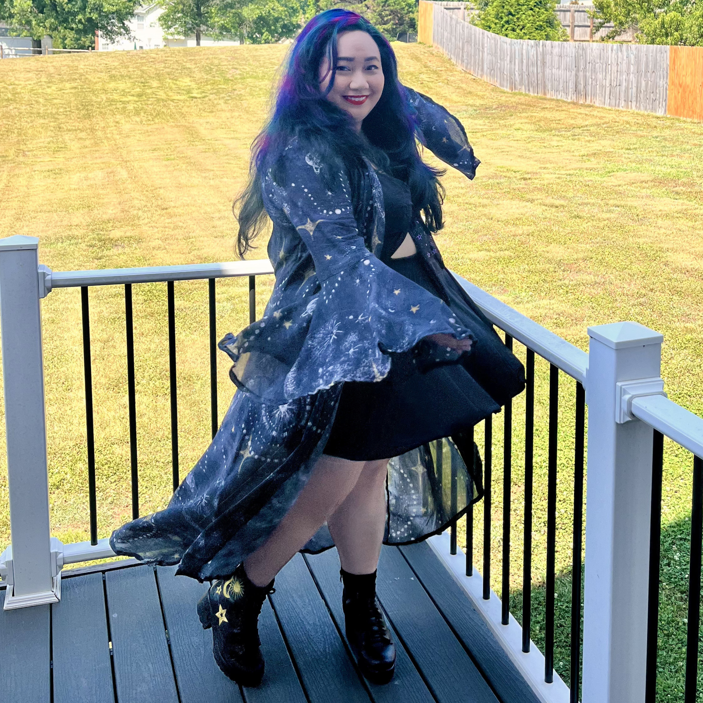 Woman twirling on a deck in front of a yard wearing a dress and a celestial print robe