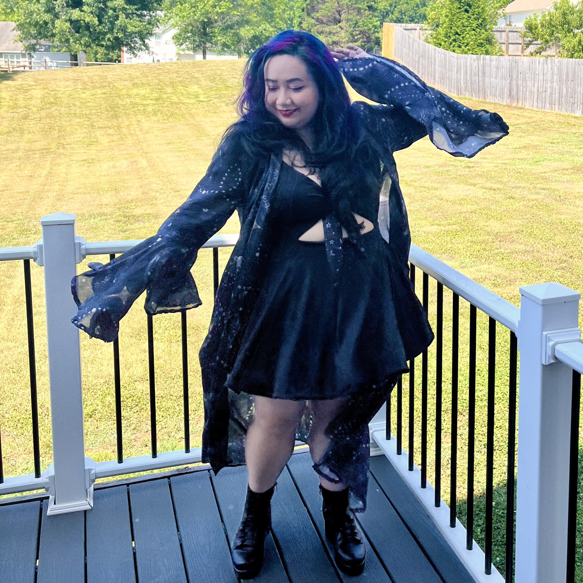Woman dancing on a deck in front of a yard wearing a dress and a celestial print robe