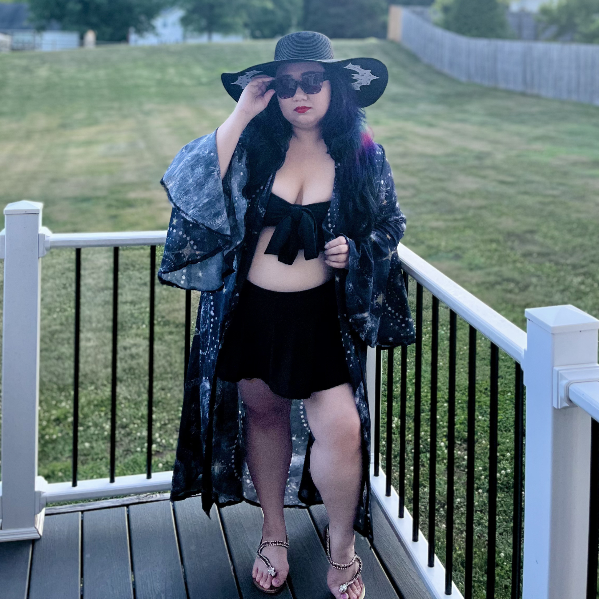 Woman standing on a deck in front of a yard wearing a bikini and a celestial print robe