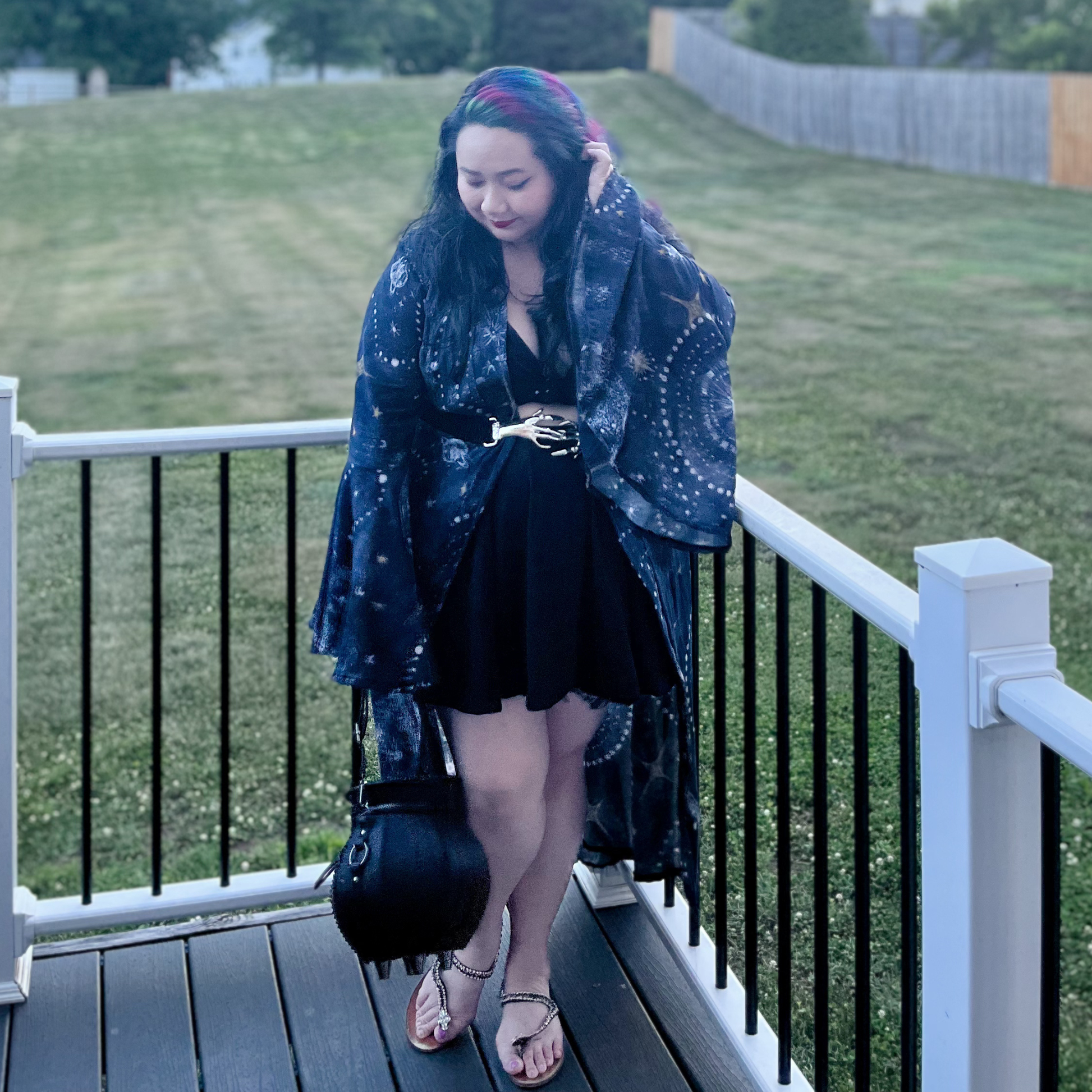 Woman standing on a deck in front of a yard wearing a dress and a celestial print robe