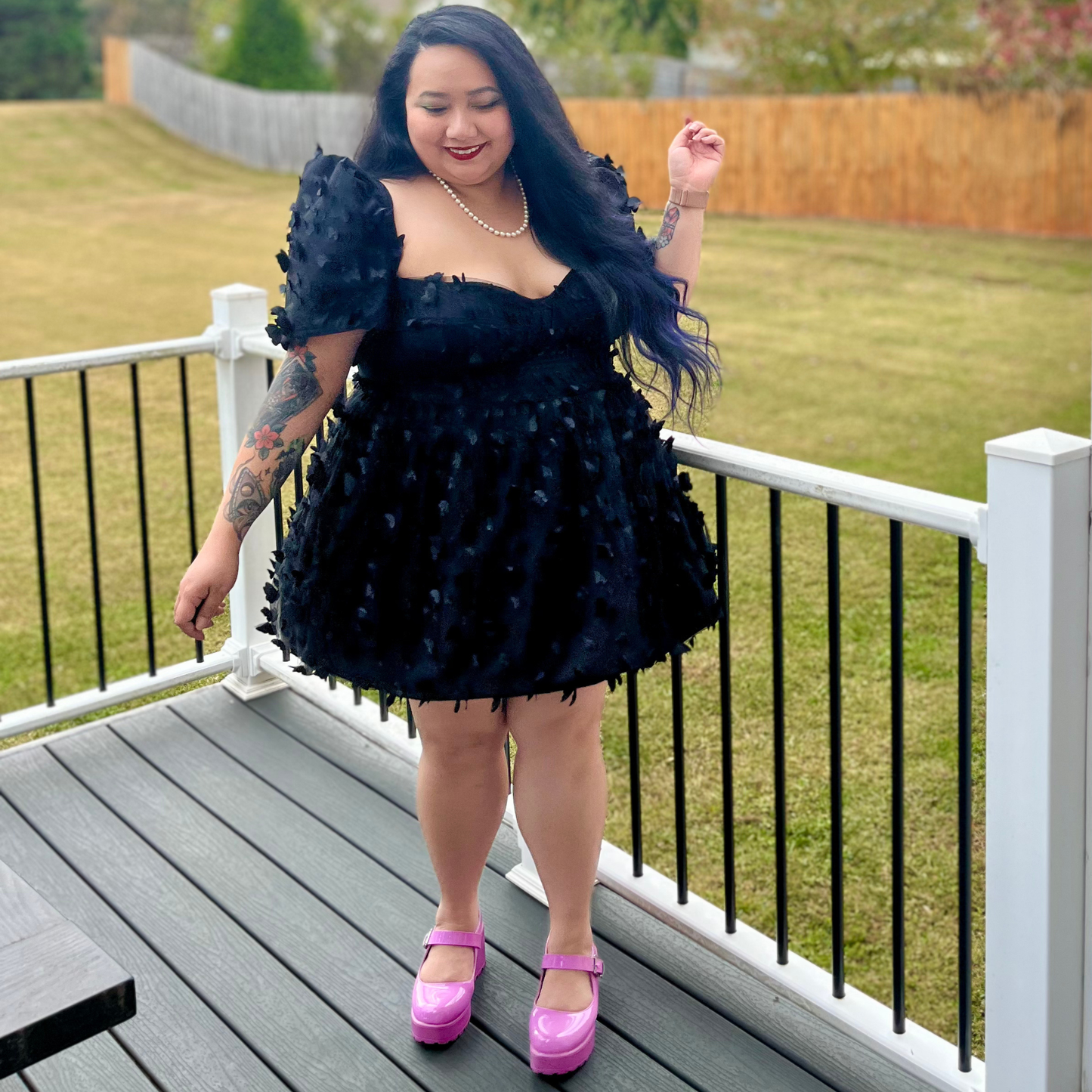 Woman in a black dress with butterfly details standing on a deck.